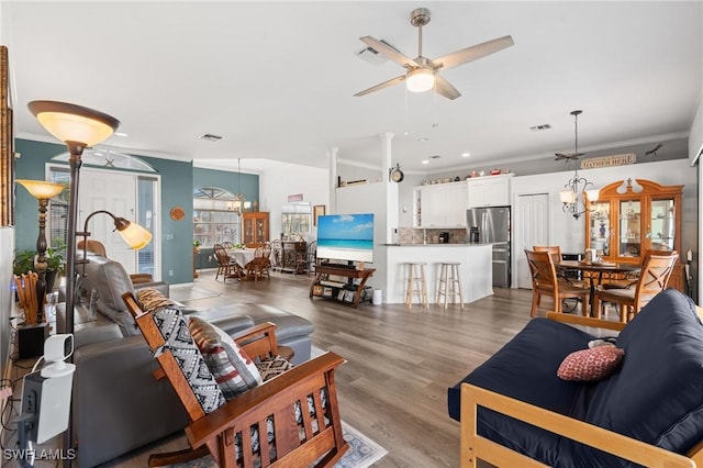 living area with visible vents, ornamental molding, wood finished floors, and ceiling fan with notable chandelier