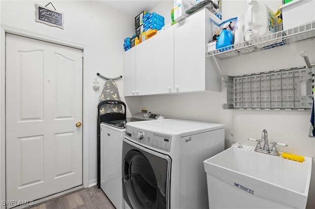 laundry area featuring cabinet space, washer and clothes dryer, a sink, and light wood finished floors