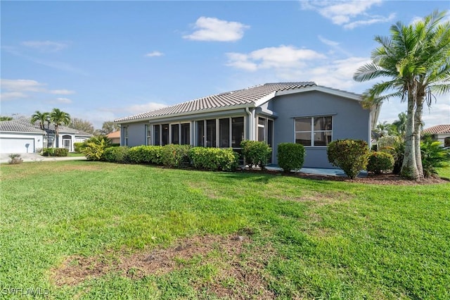 back of house featuring a sunroom, a tiled roof, a lawn, and stucco siding