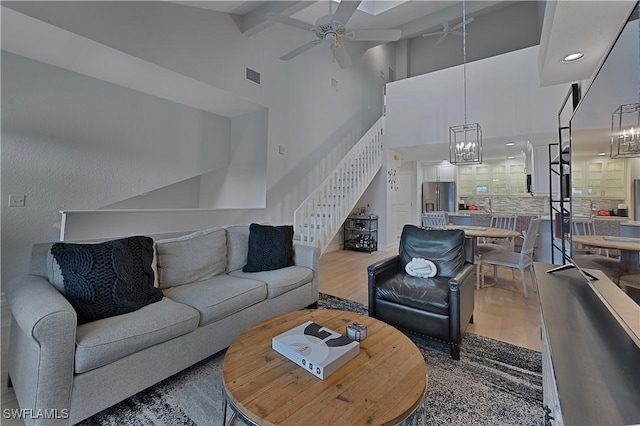 living area featuring visible vents, stairway, wood finished floors, high vaulted ceiling, and ceiling fan with notable chandelier