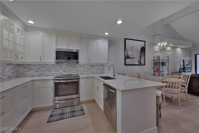 kitchen with stainless steel appliances, backsplash, white cabinets, a sink, and a peninsula