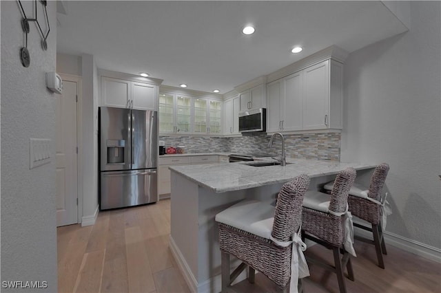 kitchen with light stone counters, appliances with stainless steel finishes, glass insert cabinets, a sink, and a peninsula