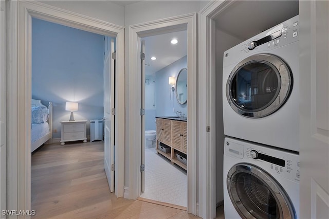 clothes washing area with light wood-style floors, stacked washer / dryer, a sink, and recessed lighting