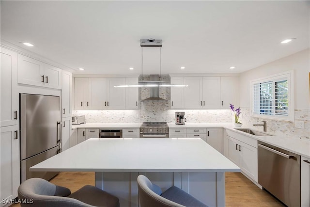 kitchen with stainless steel appliances, wall chimney exhaust hood, a sink, and a kitchen breakfast bar