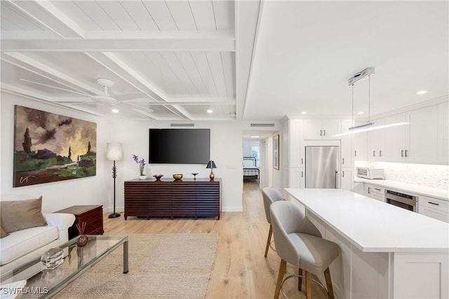 living area with beam ceiling, recessed lighting, light wood-style floors, ceiling fan, and baseboards