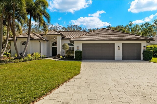 mediterranean / spanish house with decorative driveway, a tile roof, stucco siding, an attached garage, and a front yard