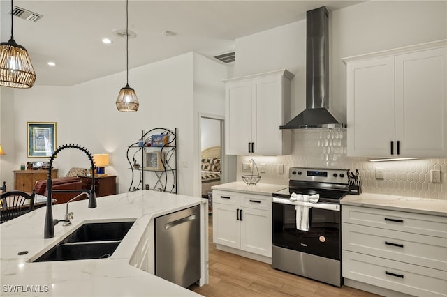 kitchen featuring visible vents, appliances with stainless steel finishes, a sink, wall chimney range hood, and backsplash