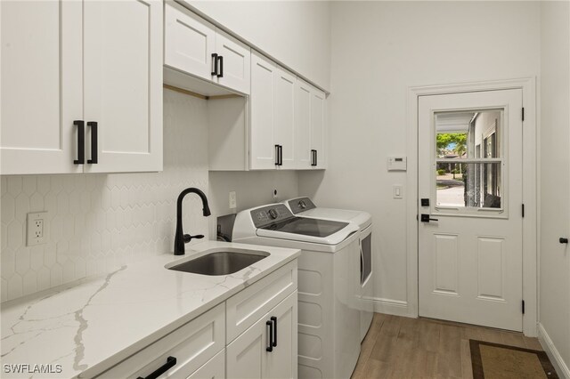 clothes washing area featuring washer and clothes dryer, cabinet space, light wood-style floors, a sink, and baseboards