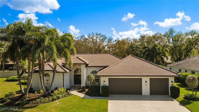 mediterranean / spanish house with a tiled roof, an attached garage, decorative driveway, a front lawn, and stucco siding