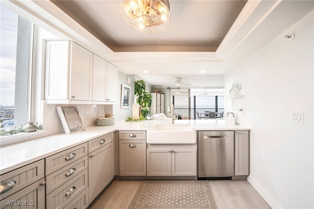 kitchen with a raised ceiling, stainless steel dishwasher, a sink, and light wood-style flooring