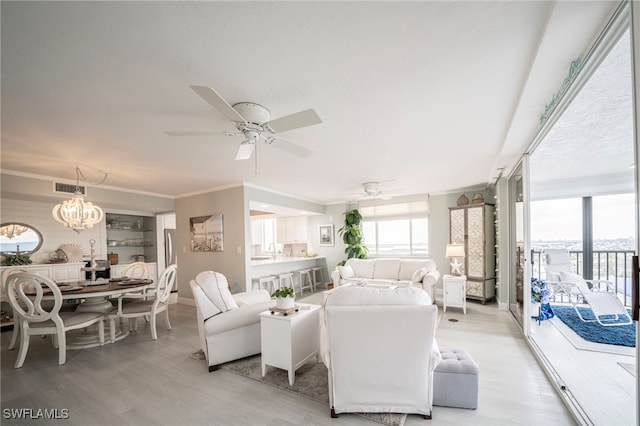 living area featuring visible vents, baseboards, light wood-style flooring, ornamental molding, and ceiling fan with notable chandelier