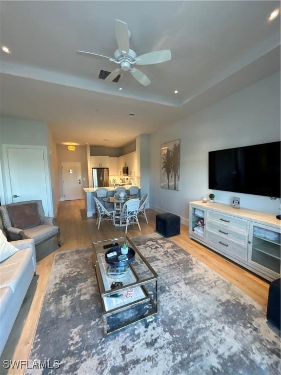 living area with light wood-style flooring, a tray ceiling, ceiling fan, and recessed lighting