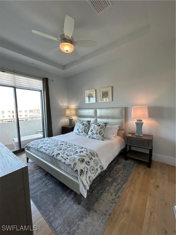 bedroom featuring access to outside, a raised ceiling, visible vents, and light wood-style floors