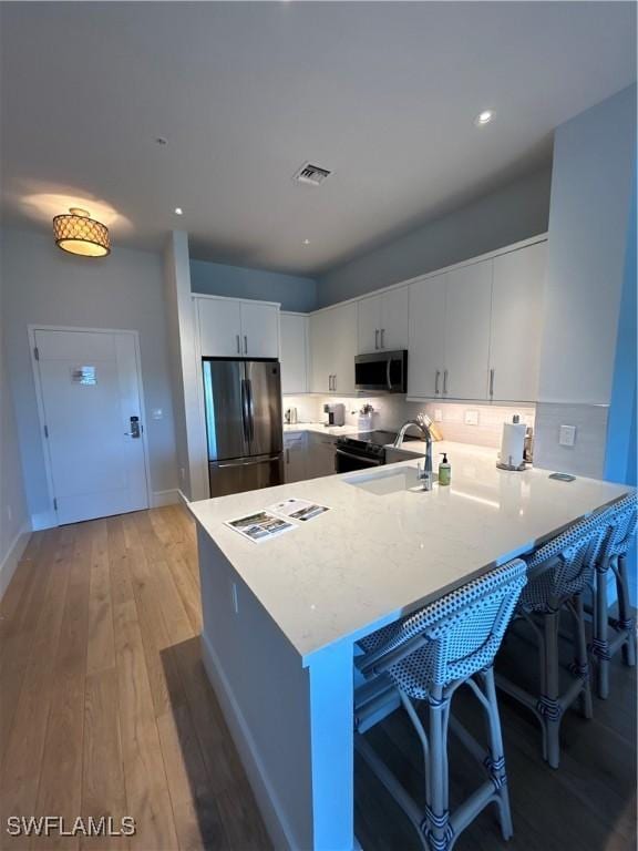 kitchen featuring visible vents, appliances with stainless steel finishes, a sink, light wood-type flooring, and a peninsula