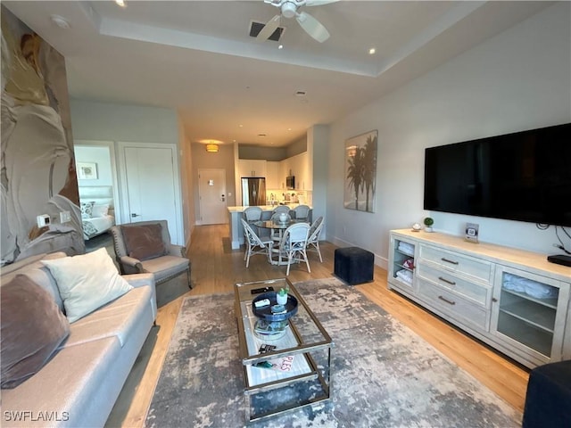 living room featuring light wood finished floors, ceiling fan, visible vents, and a raised ceiling