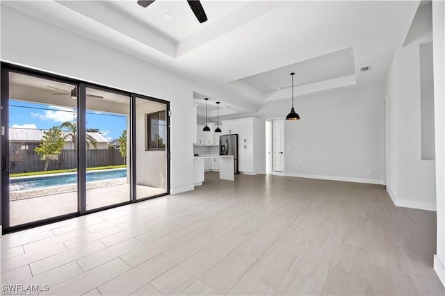 unfurnished living room with a tray ceiling, baseboards, visible vents, and a ceiling fan