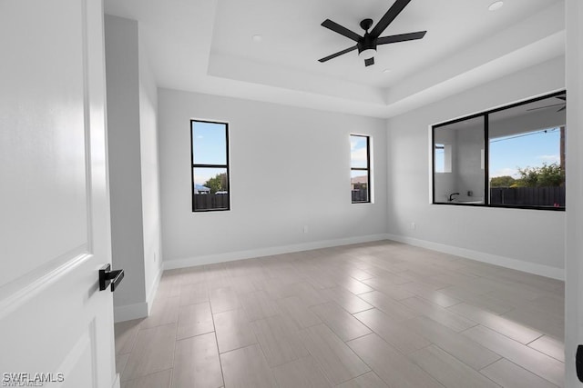 empty room with baseboards, a raised ceiling, and ceiling fan