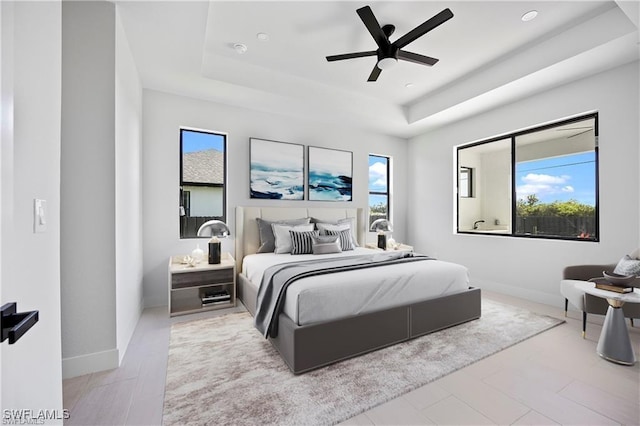 bedroom with multiple windows, a raised ceiling, baseboards, and a ceiling fan