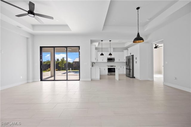 unfurnished living room with ceiling fan, baseboards, and a tray ceiling