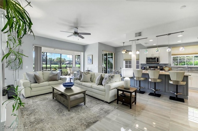 living room with a ceiling fan, visible vents, and a healthy amount of sunlight