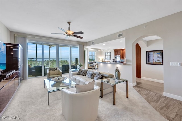 living room with baseboards, visible vents, ceiling fan, arched walkways, and light carpet