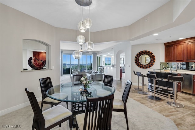 dining area with a chandelier, light wood-type flooring, arched walkways, and baseboards