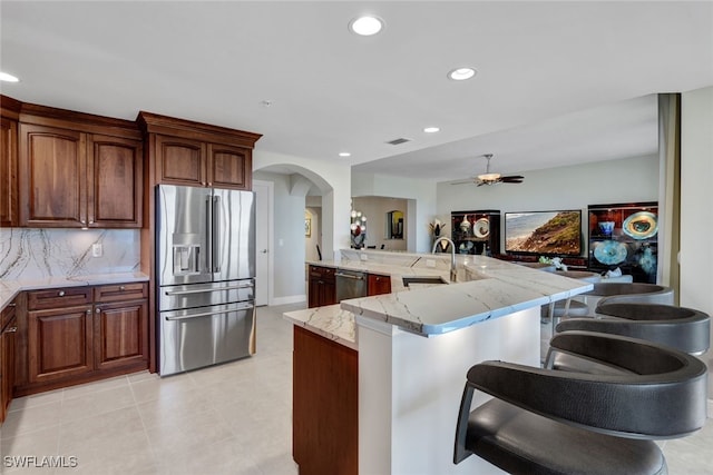 kitchen featuring a sink, stainless steel appliances, a breakfast bar area, arched walkways, and a ceiling fan
