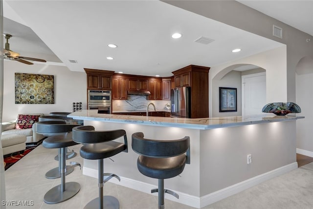 kitchen featuring ceiling fan, visible vents, a kitchen breakfast bar, stainless steel appliances, and tasteful backsplash
