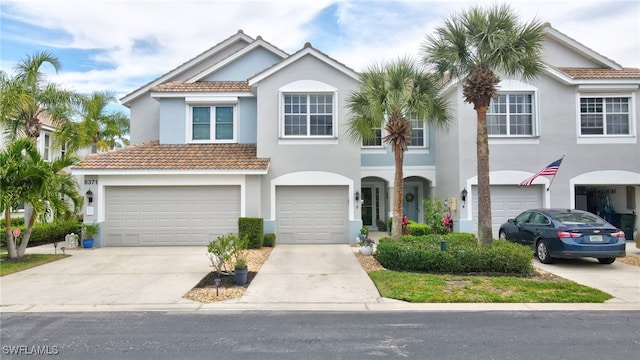 townhome / multi-family property with a garage, driveway, a tiled roof, and stucco siding