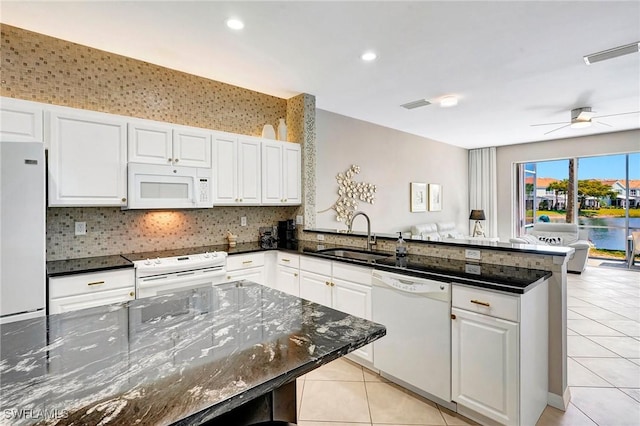 kitchen featuring light tile patterned flooring, a peninsula, white appliances, a sink, and white cabinets