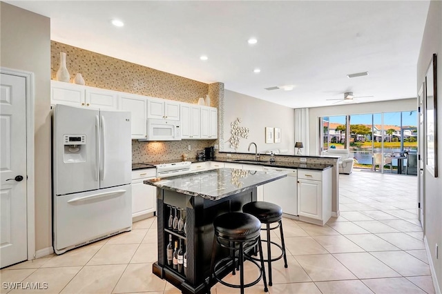 kitchen with light tile patterned floors, a peninsula, white appliances, a sink, and a center island