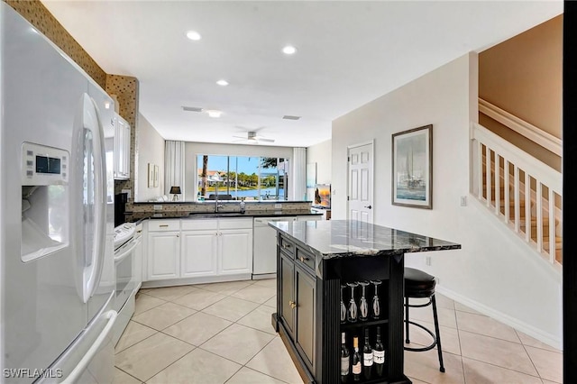 kitchen featuring light tile patterned flooring, white appliances, a breakfast bar, a sink, and dark stone countertops