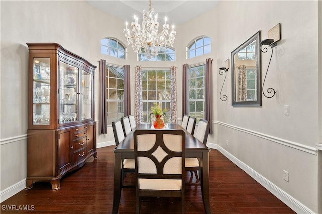 dining area featuring a chandelier, dark wood-type flooring, baseboards, and a towering ceiling