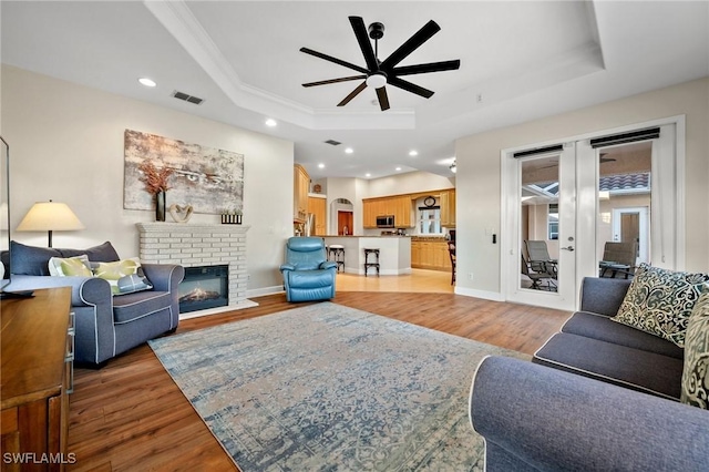 living room with light wood-style flooring, french doors, a raised ceiling, and a ceiling fan