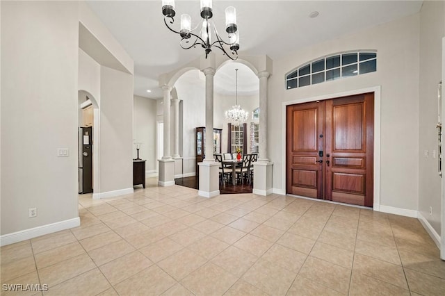 entrance foyer with ornate columns, light tile patterned floors, baseboards, and an inviting chandelier