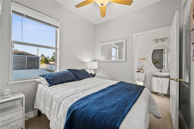 bedroom with baseboards, ensuite bathroom, tile patterned floors, a ceiling fan, and a sink