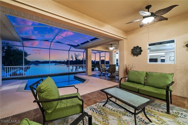 patio terrace at dusk with glass enclosure, outdoor dining space, ceiling fan, a water view, and an outdoor hangout area