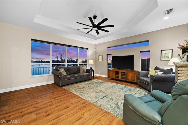 living area with visible vents, a raised ceiling, wood finished floors, and a ceiling fan