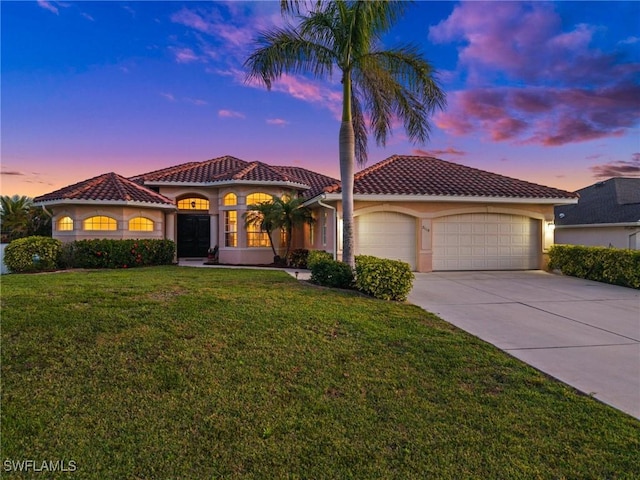 mediterranean / spanish-style home with an attached garage, a tile roof, a front yard, stucco siding, and driveway