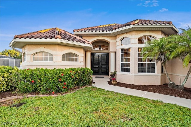 mediterranean / spanish house with a front yard, a tiled roof, and stucco siding