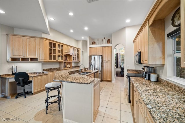 kitchen with a breakfast bar, light brown cabinets, a sink, appliances with stainless steel finishes, and stone counters