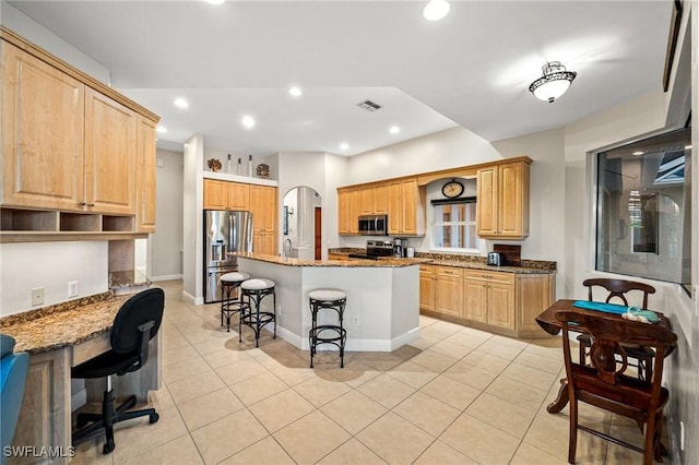 kitchen featuring stone countertops, a kitchen breakfast bar, appliances with stainless steel finishes, and light tile patterned floors