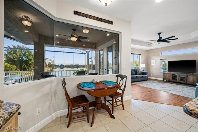 tiled dining room with a raised ceiling, baseboards, and ceiling fan