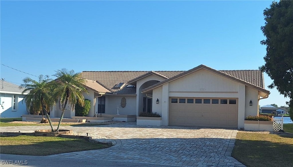 view of front facade featuring a garage, a tile roof, decorative driveway, and stucco siding