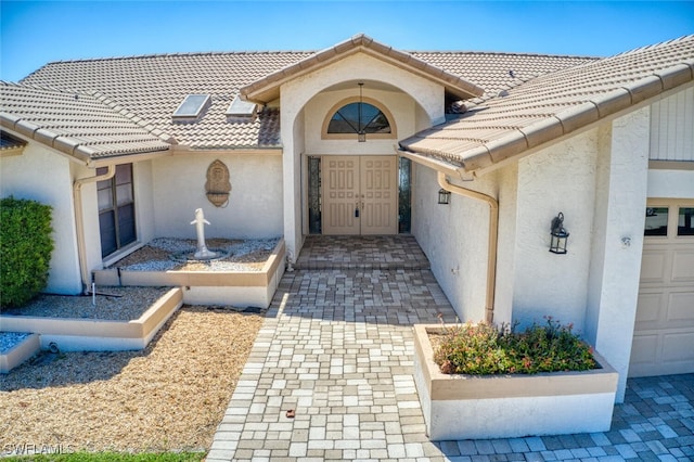 view of exterior entry featuring a garage, a tiled roof, and stucco siding