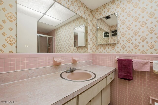 bathroom with wallpapered walls, a stall shower, wainscoting, vanity, and tile walls