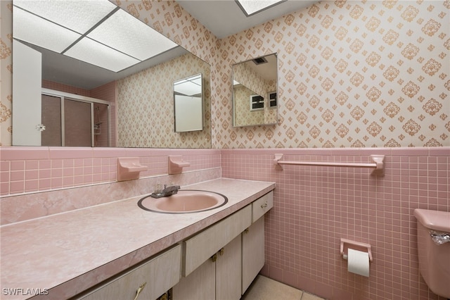 full bath featuring wallpapered walls, a stall shower, a wainscoted wall, tile patterned flooring, and vanity