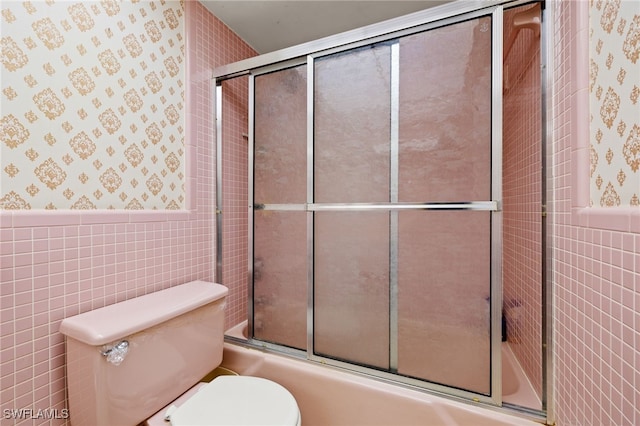 full bath featuring a wainscoted wall, tile walls, combined bath / shower with glass door, and wallpapered walls