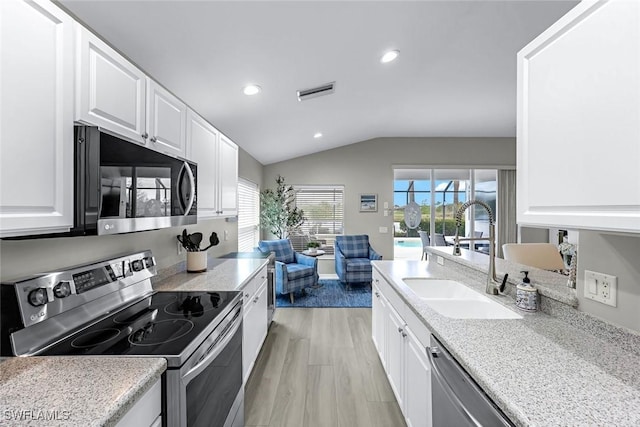 kitchen featuring stainless steel appliances, visible vents, white cabinets, vaulted ceiling, and a sink