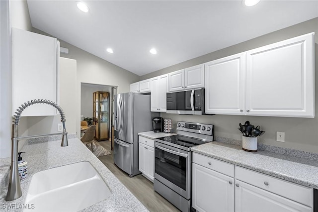 kitchen with white cabinetry, appliances with stainless steel finishes, vaulted ceiling, and a sink